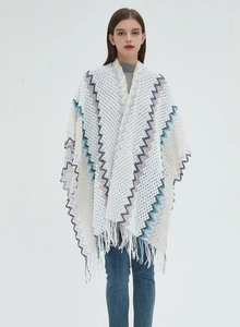 Detail of white knit poncho featuring colorful zigzag wave patterns and fine fringe trim
