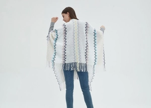 Detail of white knit shawl featuring colorful wavy patterns and long fringe tassels