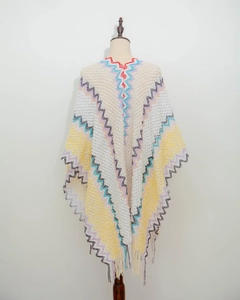 Detailed view of white knitted poncho with colorful ethnic zigzag patterns and fringe on mannequin