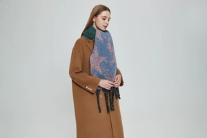 Detailed view of thick knit scarf with star patterns and chunky tassels on camel wool coat