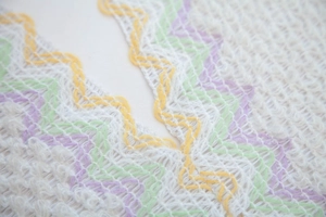 Detail of white knit shawl showing colorful wavy edges and delicate mesh texture