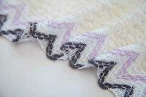 Macro detail of white knit shawl showing mesh texture and purple zigzag stitched edge
