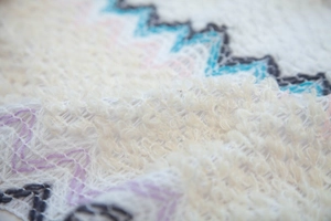 Macro shot of white knitted shawl texture with colorful wavy zigzag pattern and soft fringe
