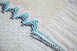 Detail of white knit shawl with colorful wavy patterns and soft fringe trim