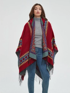 Détail du poncho bohème rouge avec motifs de cœur colorés et pompons noirs