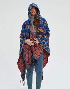 Front view of hooded poncho featuring geometric patterns, royal blue knit and fringe trim