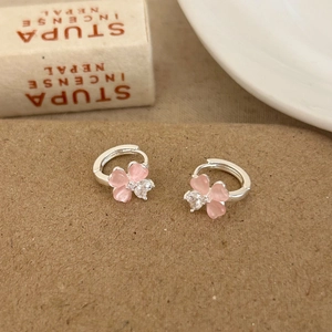 Detail of pink cat-eye stone flower earrings with heart-shaped zircon on textured brown paper