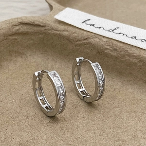 Close-up of silver zircon hoop earrings on a textured handmade display tray