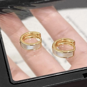 Close-up of golden hoop earrings featuring white shell inlay on a black surface