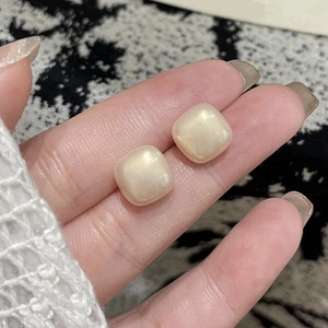 Minimalist square rounded pearl stud earrings held between fingers for size reference