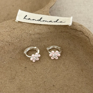 Vue détaillée de boucles d'oreilles fleur rose avec zircon central sur carte artisanale