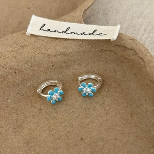 Détail de créoles argentées avec fleurs en émail bleu ciel et centres en zircon