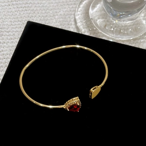 Macro detail of 18K gold-plated open bangle with red heart zircon and micro-pave setting