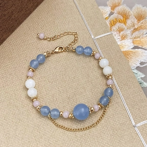 Detail of natural stone beaded bracelet with gold chain, tassels, and elegant floral accents