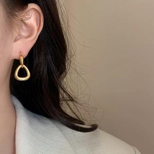 Minimalist geometric gold drop earrings featuring a polished triangular pendant on model