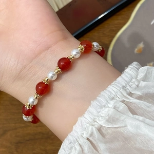 Mano con bracciale di agata rossa e perle con accenti dorati su una scrivania di legno