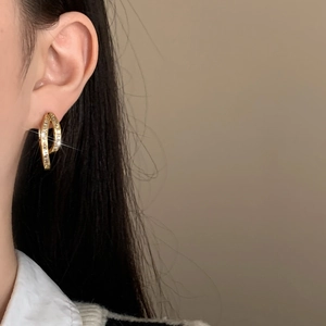 Detail of gold-plated crossover hoop earrings with shimmering cubic zirconia stones