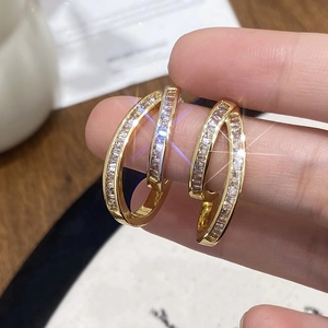 Golden C-shaped earrings with rectangular zircons shown being held by hand