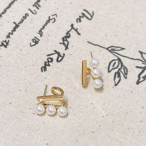 Elegant gold bar stud earrings featuring three pearls on a vintage linen backdrop