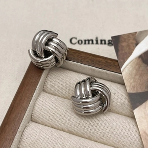 Detailed close-up of silver knot stud earrings on a beige velvet jewelry display