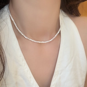 Close-up of minimalist tiny white pearl choker necklace worn by a model on white outfit