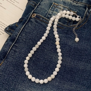 Detail of white beaded necklace with silver clasp on dark blue denim fabric background