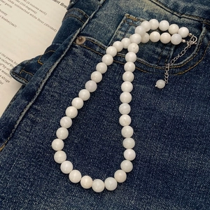 Detail of white beaded necklace with silver lobster clasp on denim fabric backdrop