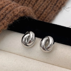 Polished silver double twisted knot geometric stud earrings on canvas background
