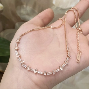 Rose gold necklace with baguette-cut zircons held by hand against a floral background