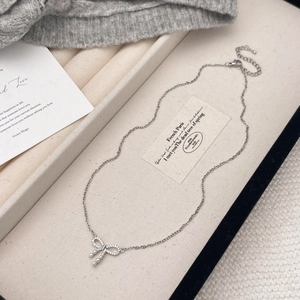 Detailed view of silver bow necklace with micro-pave crystals and dangling pearls