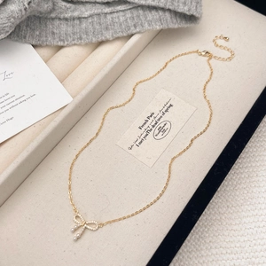 Gold bow pendant necklace with micro-pave cubic zirconia and three pearls on a jewelry box