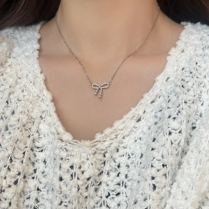 Detail of zircon bow pendant necklace with pearl on a white knit sweater model
