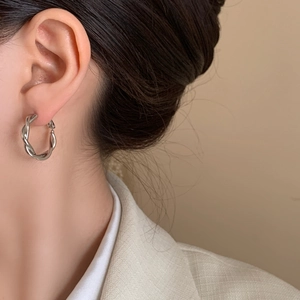 Silver twisted hoop earrings with a textured woven design worn by a female model
