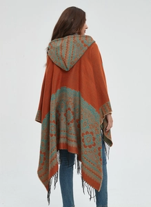 Détail d'un poncho en maille à capuche avec jacquard floral et finitions de franges