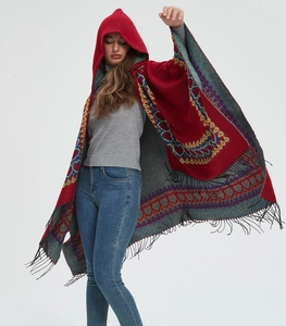 Détail d'un poncho rouge à capuche avec motifs ethniques et bordure à franges noires