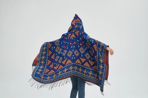 Detail view of hooded poncho featuring royal blue knit with geometric patterns and fringe