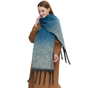 Thick ombre blue knit scarf with chunky tassels over a camel coat on white background