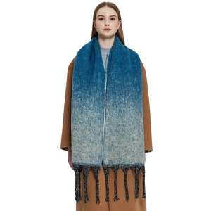 Blue-grey gradient knit scarf with thick black tassels on a model in a brown coat