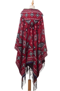 Detail of red geometric jacquard hooded cloak with long black fringe tassels at the hem