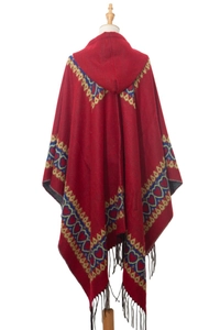 Détail d'un poncho rouge à capuche avec motifs de cœur et bordure à franges noires