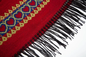 Détail d'un poncho en tricot rouge avec motifs de cœur bleus et franges noires