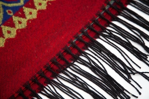 Détail d'un châle ethnique rouge avec motifs géométriques et pompons noirs élégants
