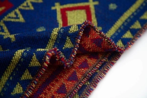 Detail of blue knitted hooded poncho featuring ethnic geometric patterns and thick texture