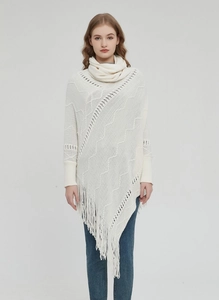 Detail eines cremefarbenen Strickponchos mit Hohlwellenmustern und langen Fransen