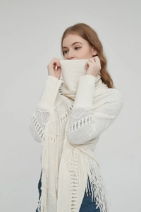 Detailaufnahme von cremefarbenem Strickponcho mit Hohlmustern und langen Zierquasten