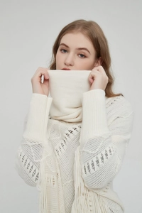 Nahaufnahme von cremeweißem Strickponcho mit Hohlmustern und Quastenverzierung am Saum