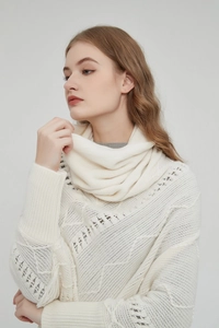 Detail eines cremefarbenen Strickponchos mit Hohlmustern und Fransenverzierung