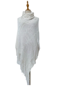 Detail eines weißen Strickponchos mit Rollkragen, Quasten und Wellenstrickmustern