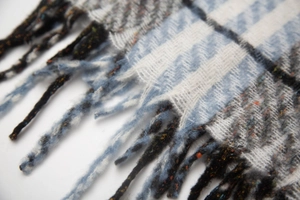 Close-up of sky blue plaid scarf fabric texture with soft tassels and woven fringe