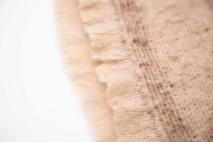 Close-up of beige knit scarf with soft tassel edges and speckled faux mohair texture